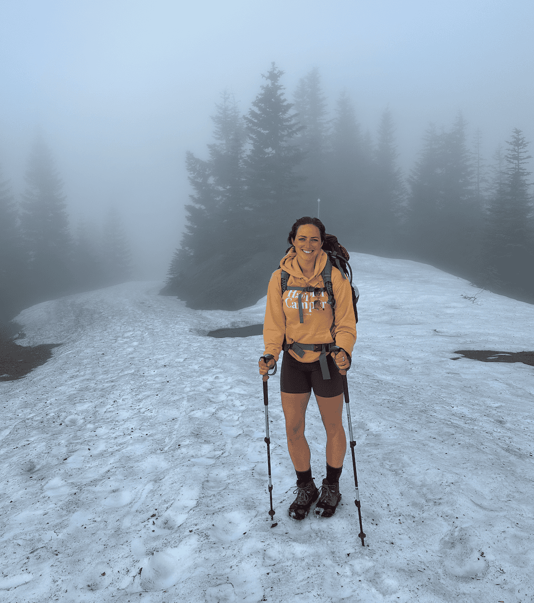 A woman standing on a snowy/icy trail in Washington State during a spring backpacking trip.
